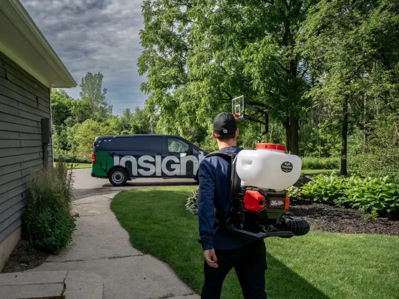 Technicien avec un pulvérisateur dorsal qui marche vers la cour